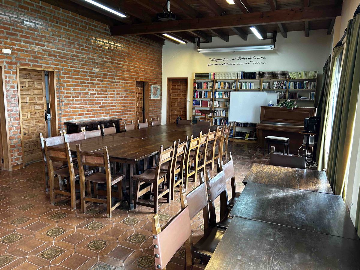 Salón con mesas de madera, estanterías con libros y un piano